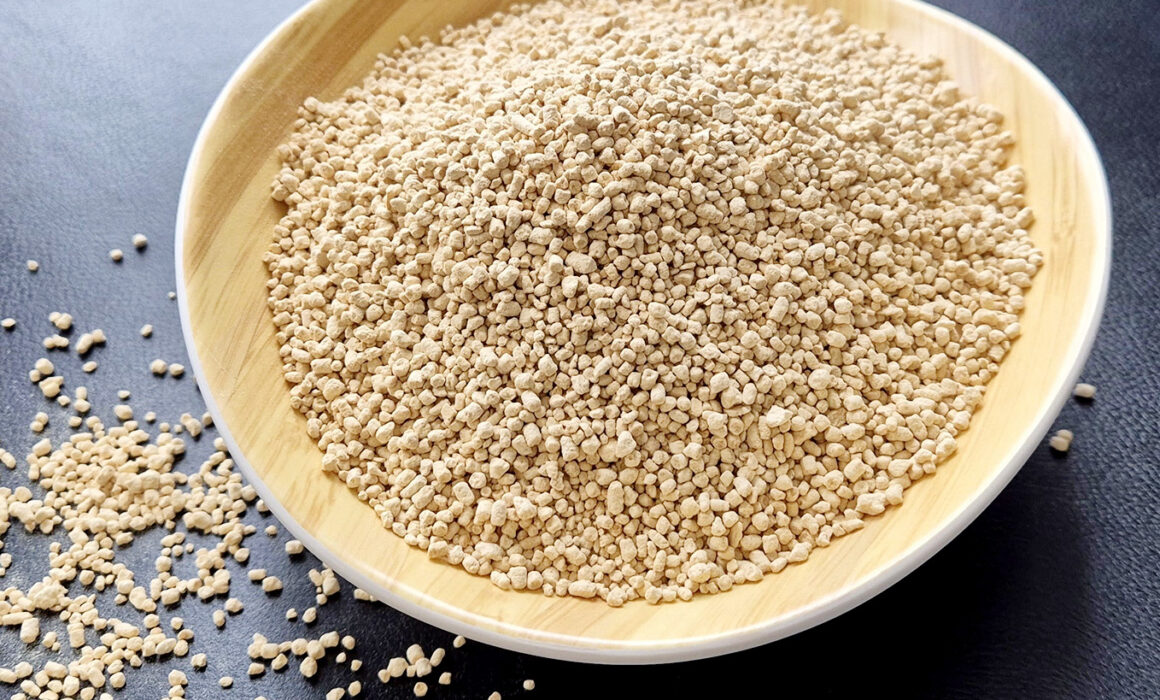 A bowl of lecithin granules in a wooden bowl on a dark table top. Some granules have fallen off and scattered to the side.
