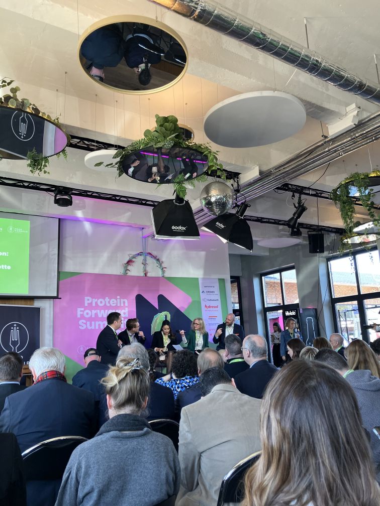 At the Protein Forward Summit: View from the audience towards the stage where 5 people are enganged in a discussion about proteins.