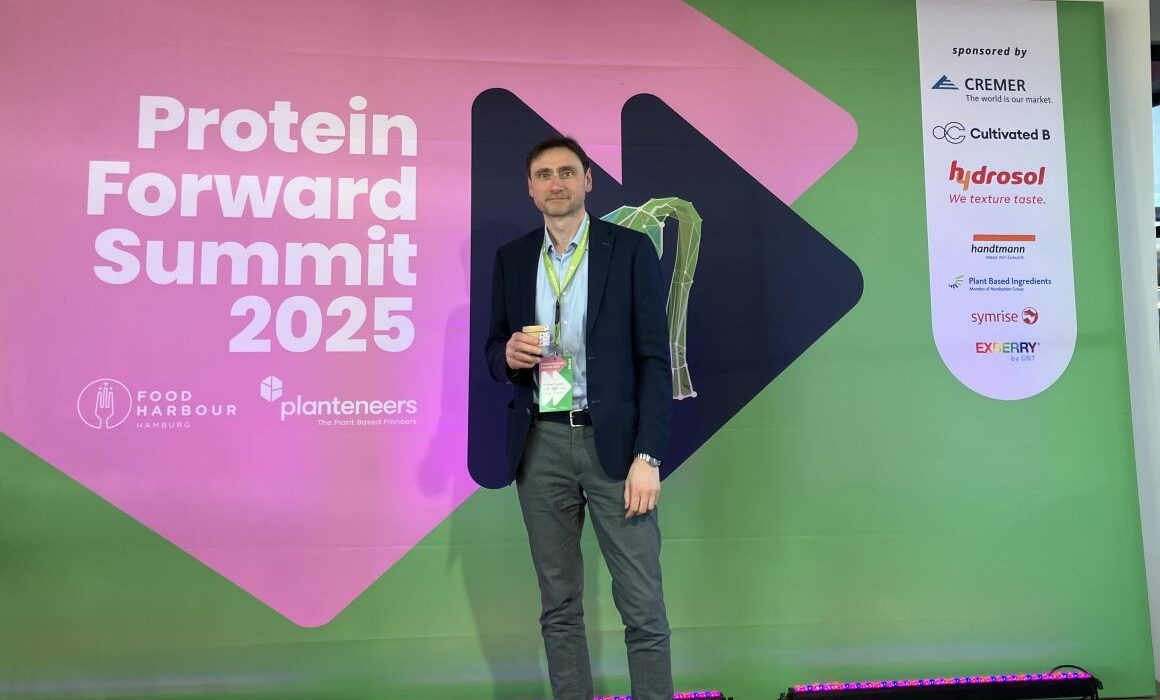 Dr. Waldemar Buxmann standing in front of the welcome banner of the Protein Forward Summit.